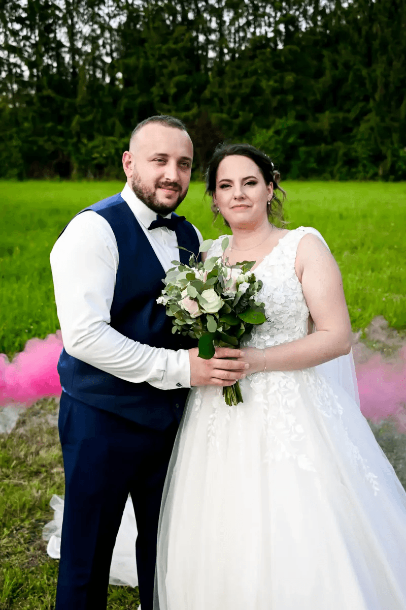 Mariés posant dans un champ avec fumée rose