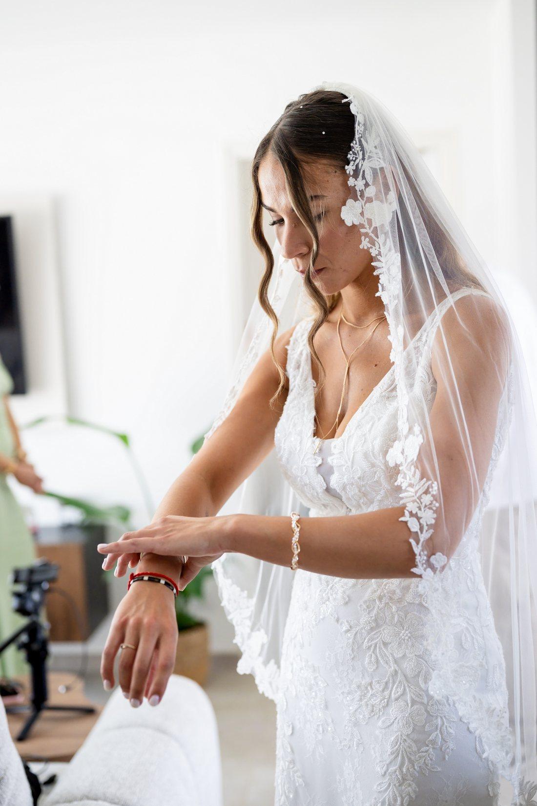 La mariée ajuste son bracelet pendant les préparatifs, voile en dentelle