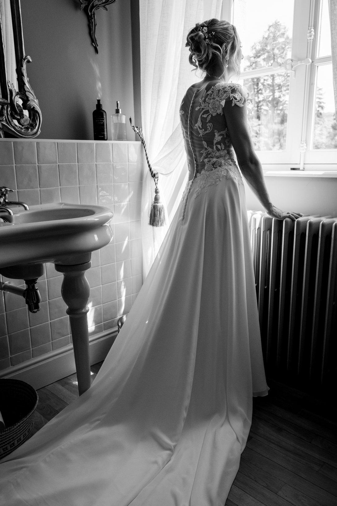 Mariée de dos pendant les préparatifs, lumière de fenêtre en noir et blanc