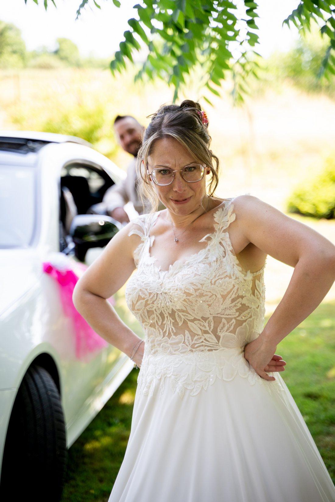 Mariée en robe de dentelle devant la voiture de mariage décorée