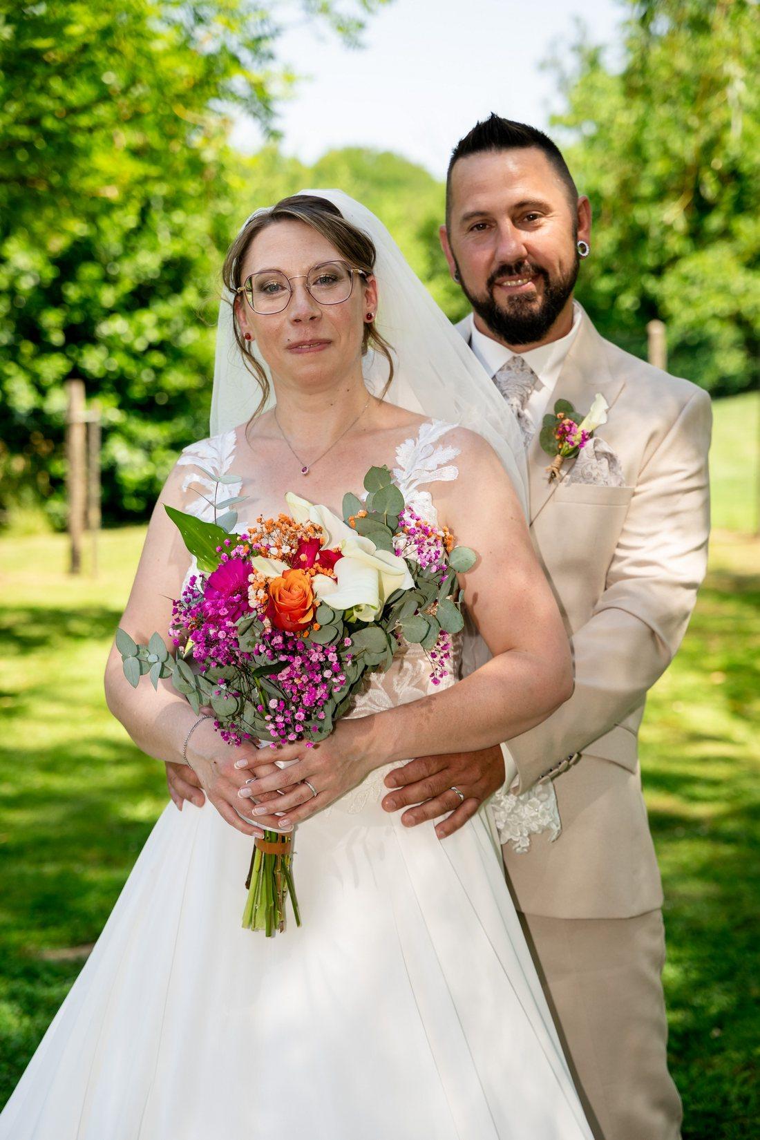 Portrait des mariés dans un jardin avec bouquet champêtre rose et orange