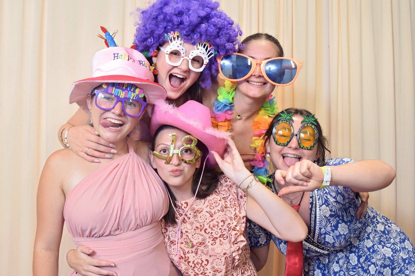 Groupe d'amies déguisées avec perruques et lunettes devant le photobooth d'un anniversaire de 18 ans
