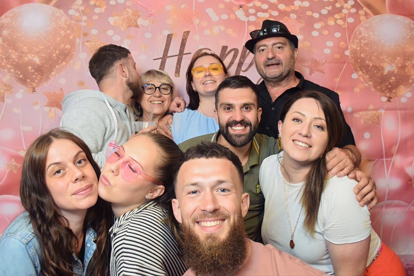 Famille posant avec des accessoires devant un fond rose Happy Birthday au photobooth d'un anniversaire