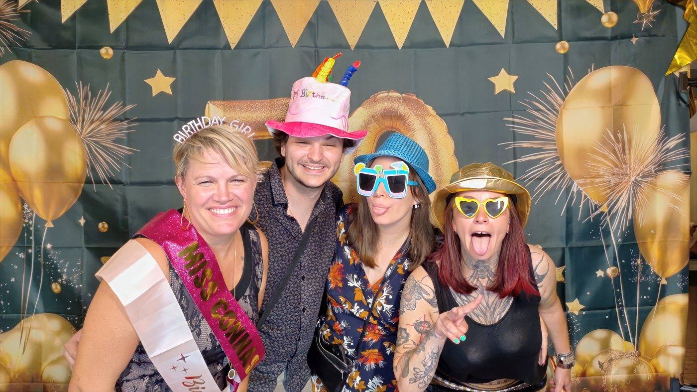 Invités déguisés avec chapeaux et lunettes devant un fond noir et doré à ballons au photobooth d'un anniversaire