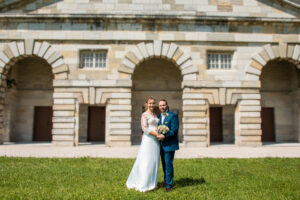 Les mariés devant les salines d'Arc-et-Senans historique avec un bouquet Mariés posant devant les salines d'Arc-et-Senans avec un bouquet