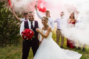 Les mariés posant avec les invités qui allument des fumigènes rouges Mariés et invités avec des fumigènes rouges allumés