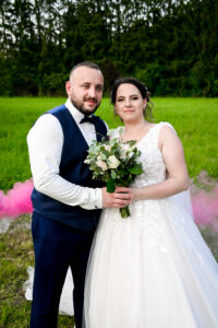 Les mariés posant dans un champ avec de la fumée rose en arrière-plan Mariés posant dans un champ avec fumée rose en arrière-plan