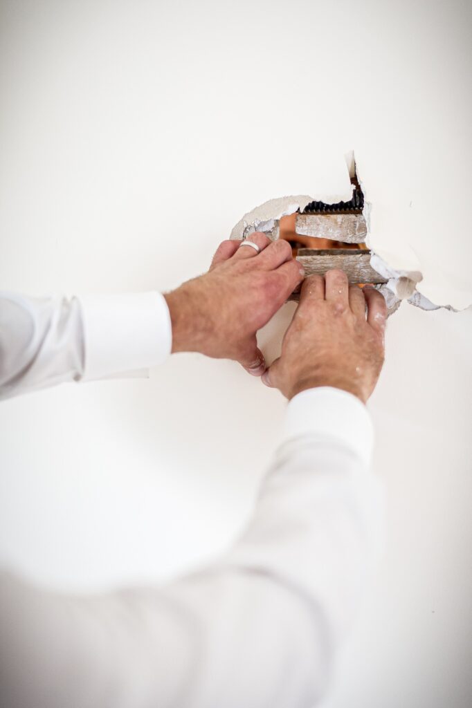 Les mains du marié arrachant le placo du mur lors d'une séance Trash the dress Mains du marié arrachant le placo du mur pendant une séance Trash the dress