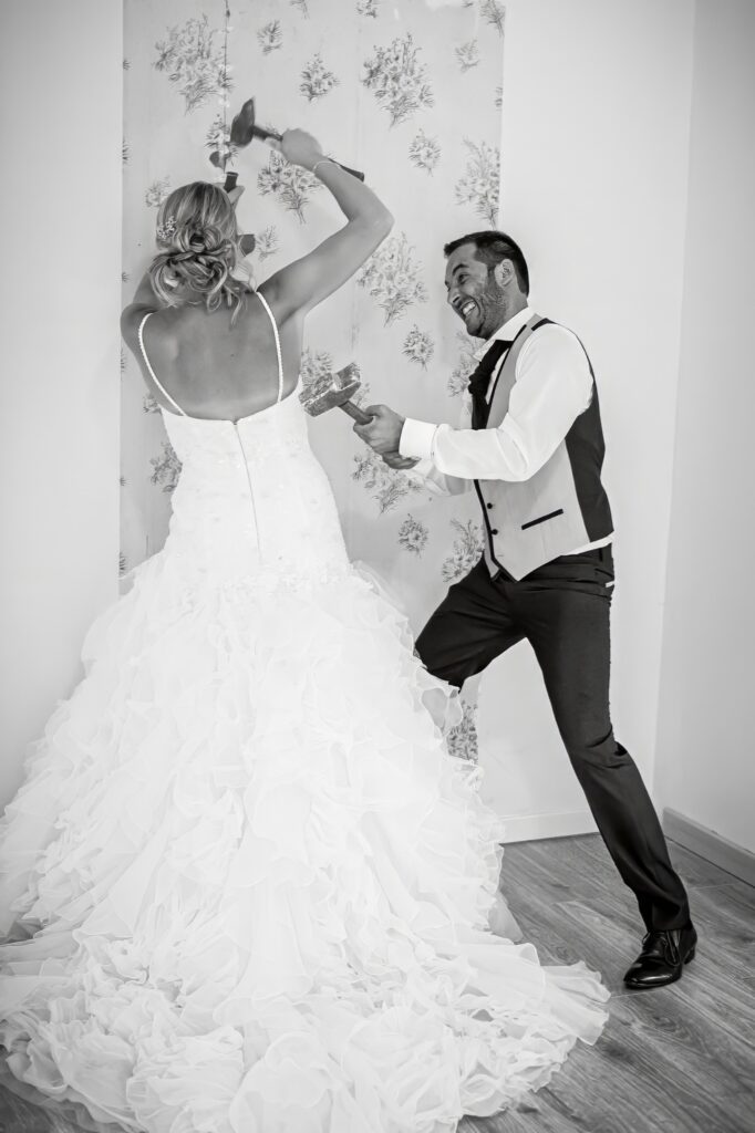 Mariés cassant un mur avec des marteaux lors d'une séance Trash the dress Couple de mariés cassant un mur ensemble avec des marteaux pendant une séance Trash the dress