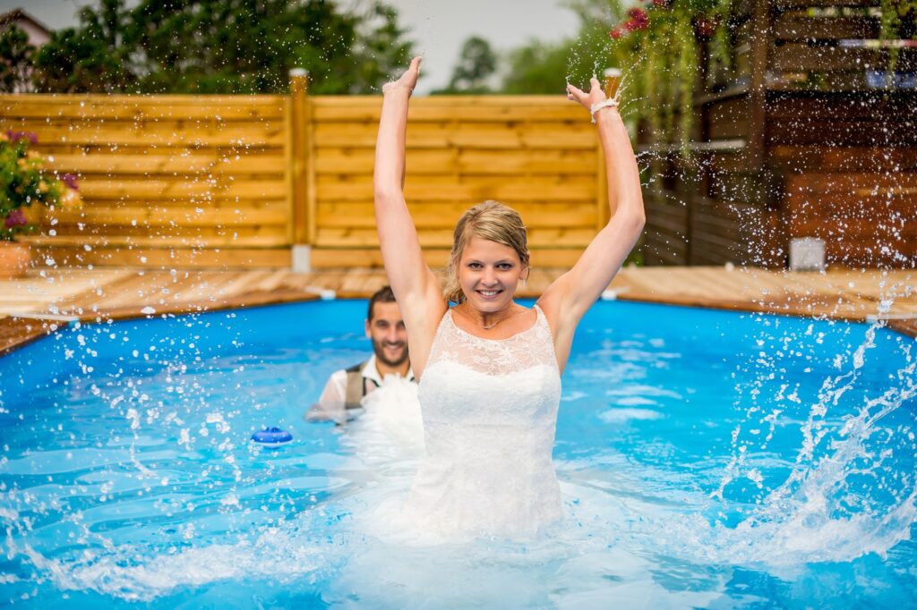 Mariés jouant dans une piscine en robe et costume lors d'une séance Trash the dress Couple de mariés jouant dans une piscine en robe de mariée et costume pendant une séance Trash the dress