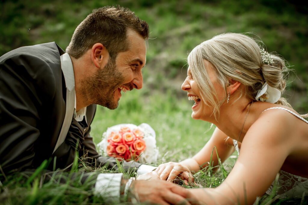Mariés riant ensemble allongés dans l'herbe lors d'une séance Trash the dress Couple de mariés riant allongés dans l'herbe pendant une séance Trash the dress