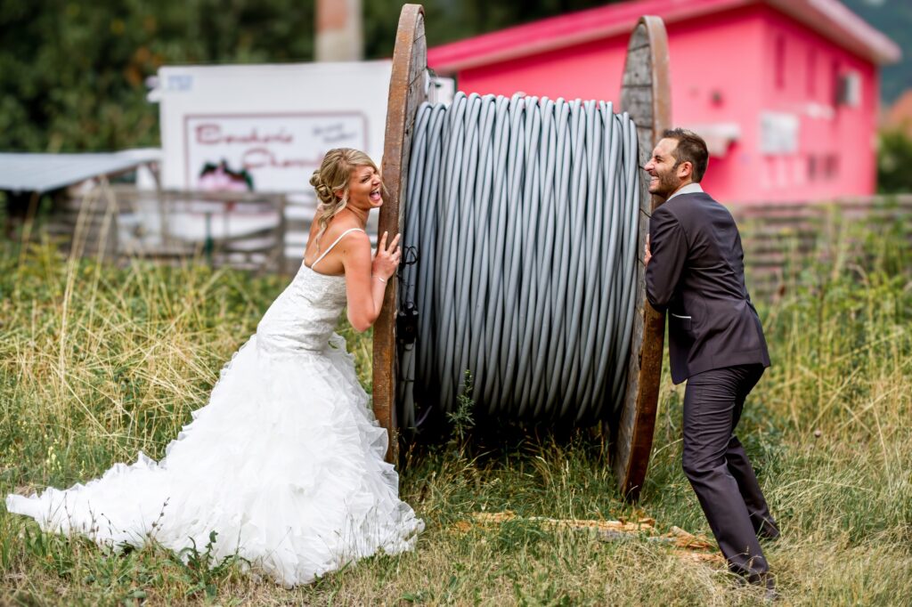 Mariés jouant avec un énorme tambour de câble en plein air lors d'une séance Trash the dress Couple de mariés s'amusant avec un énorme tambour de câble en plein air pendant une séance Trash the dress