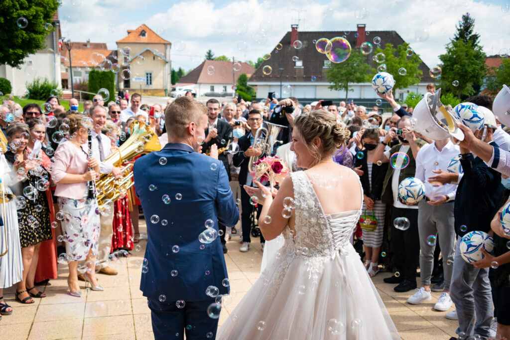 Sortie de l'église : les mariés face aux invités avec des bulles autour d'eux, vue de dos Mariés sortant de l'église avec des bulles entourant leurs silhouettes, vue de dos